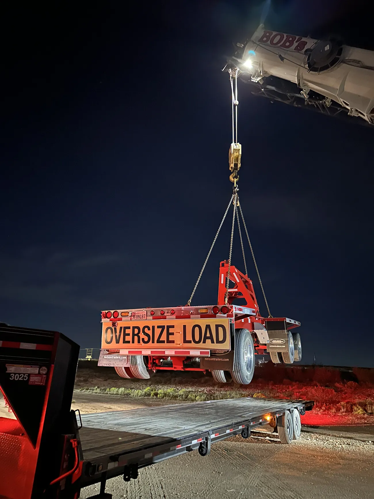Crane lifting a red trailer marked Oversize Load at night