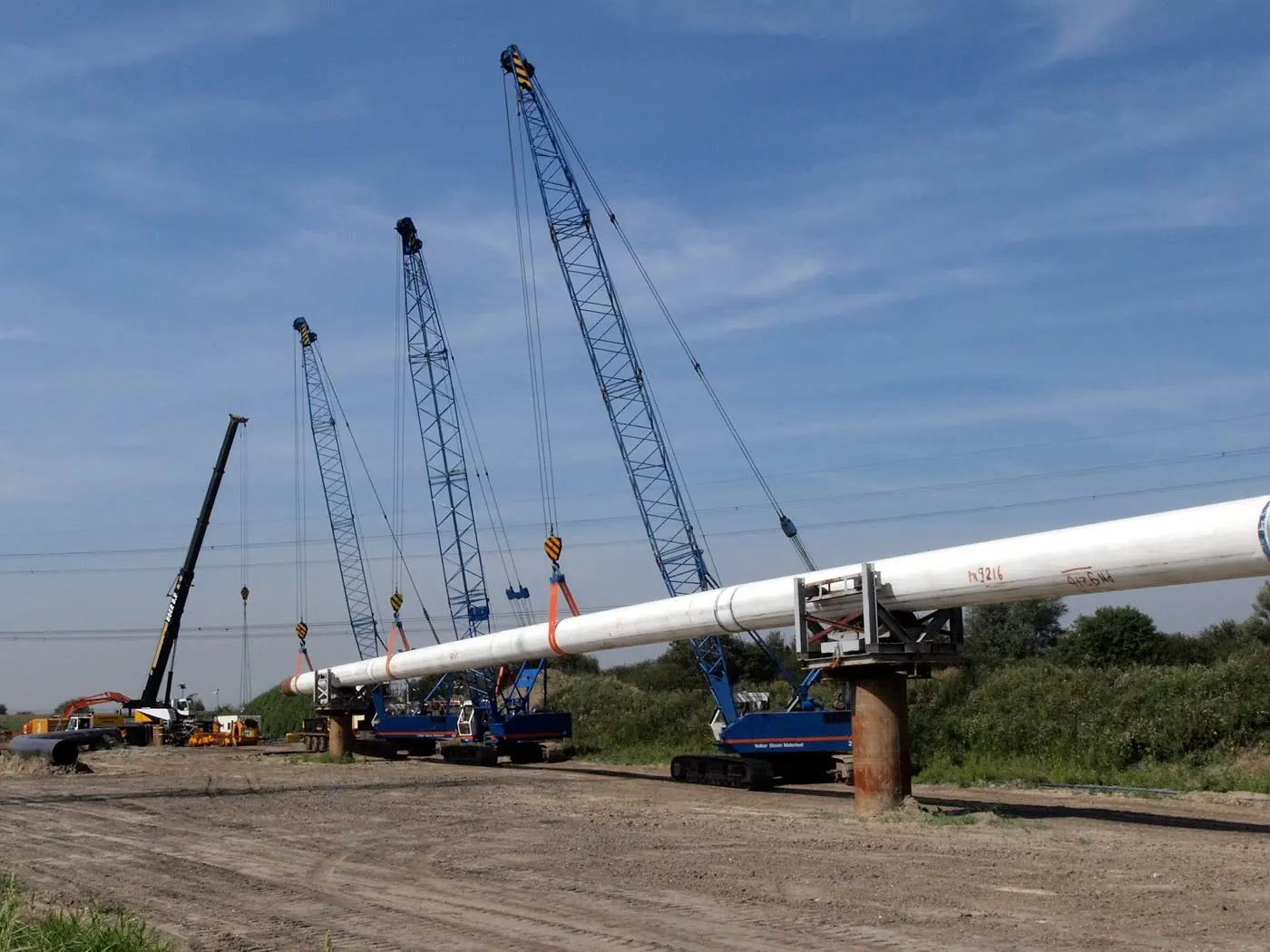 Three crawler cranes lifting a long section of pipe